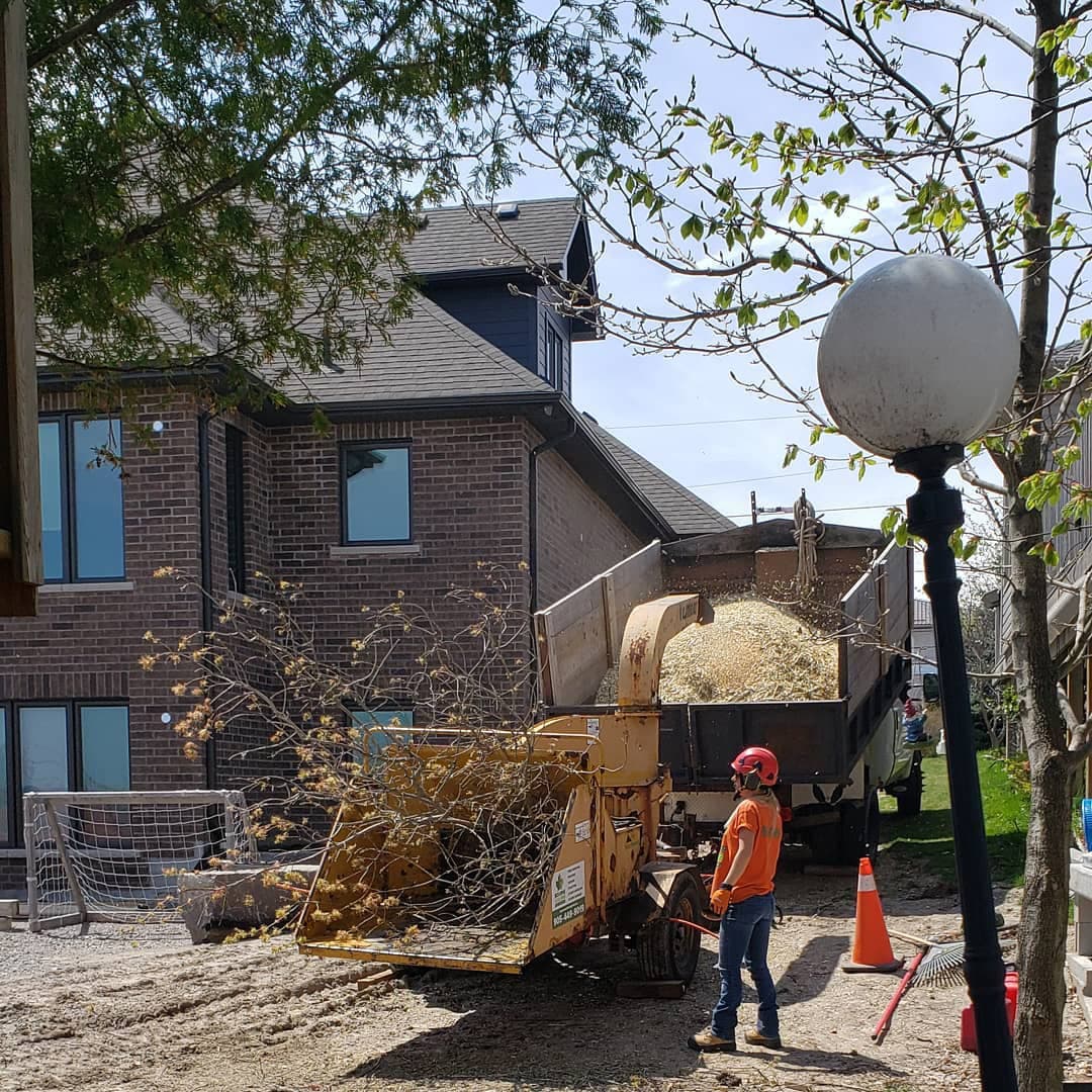 Crew chipping storm-damaged limbs into a tow-behind chipper, loading a dump trailer during residential post-storm cleanup