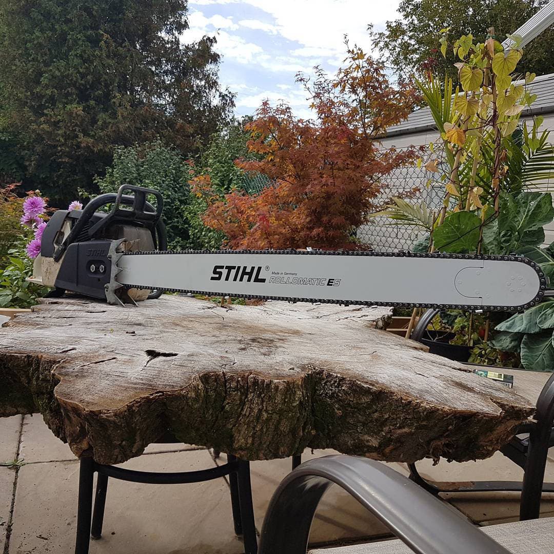 Stihl chainsaw with long bar resting on a freshly milled live-edge hardwood slab from urban tree salvage